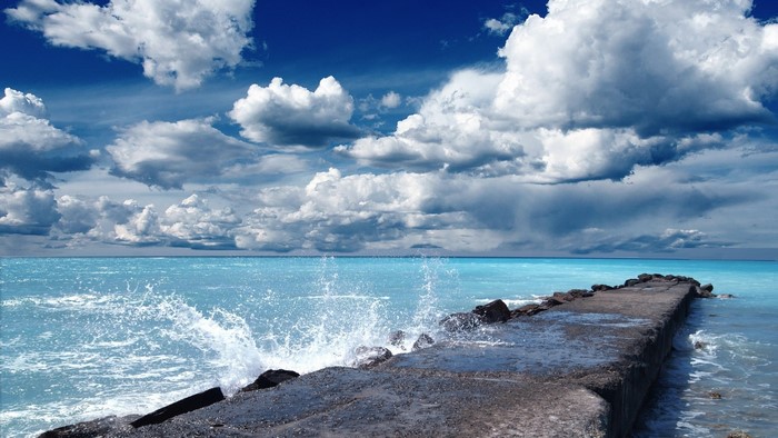 Stone dock on a bright blue sea under a cloudy sky