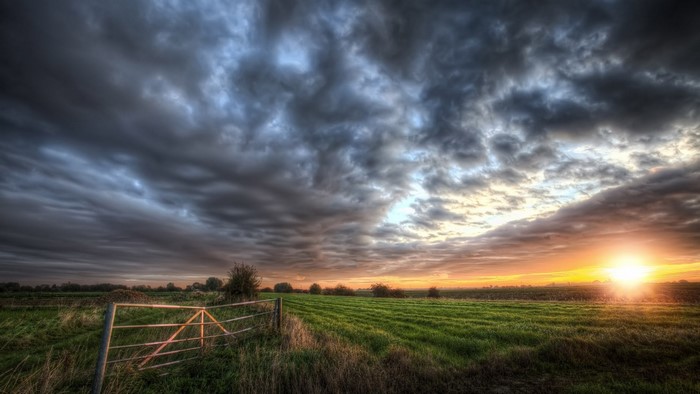 Sunset over a farm field with a fence