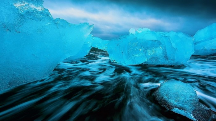 Blue icebergs on a dark beach with waves