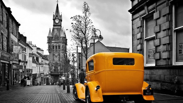 Yellow vintage car on a street with a clock tower
