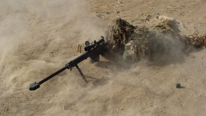 Military sniper in camouflage firing a rifle