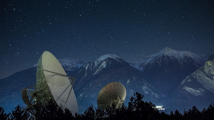 Observatory dishes under starry sky with mountains