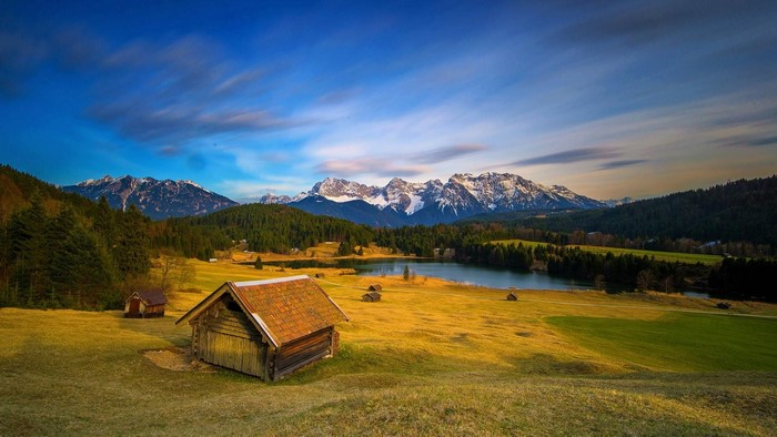 Wooden cabin by a lake with snow-capped mountains in the background