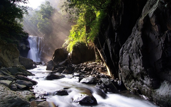Waterfall flowing through a rocky gorge with sunbeams