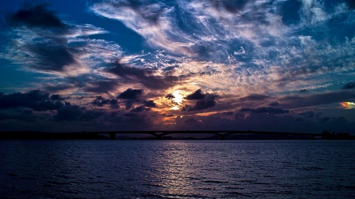 Sunset over water with bridge and clouds