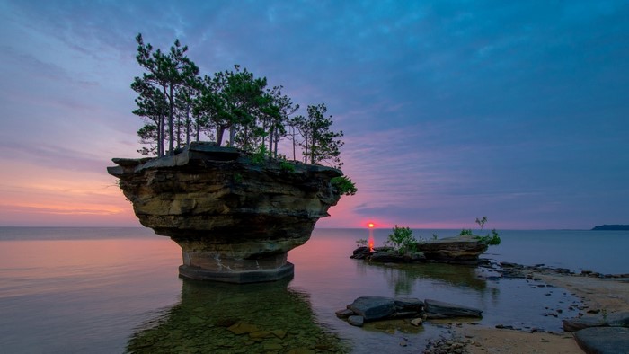 Sea stack with trees at sunrise over water