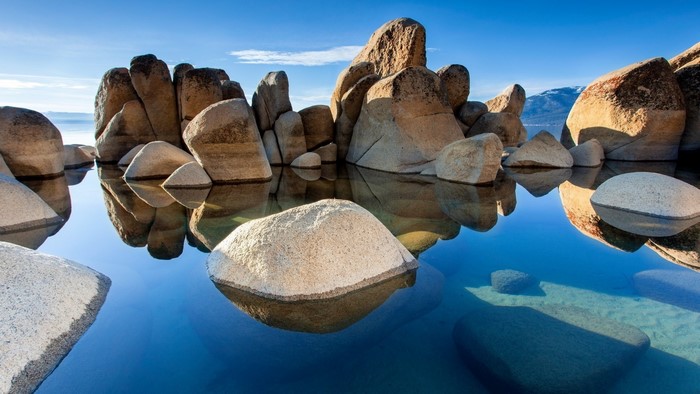 Rocky shore with clear blue water and mountain reflection