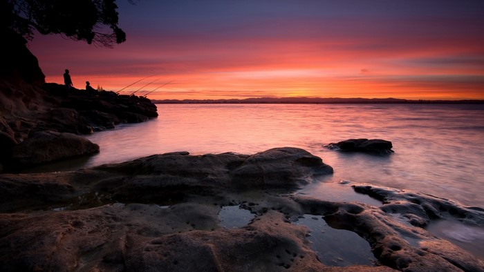 People fishing at sunset on rocky shore