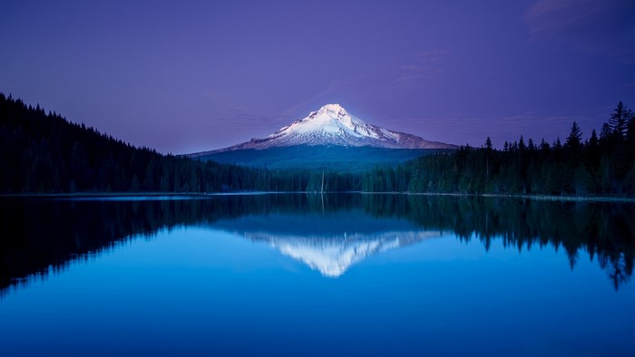 Snow-capped mountain reflected in a blue lake at dusk