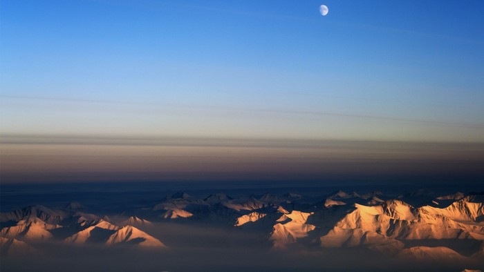 Moon over snow-capped mountains at sunset