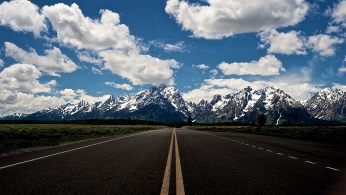 Highway leading to snow-capped mountains under a cloudy sky