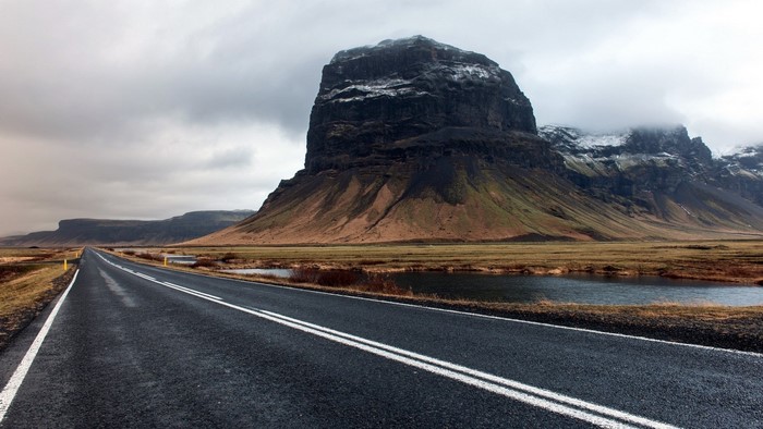 Road leading to a large mountain under a cloudy sky