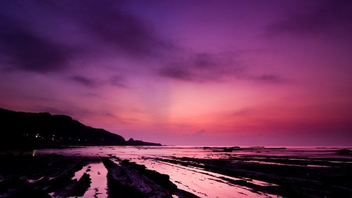 Purple sunset over rocky coastline