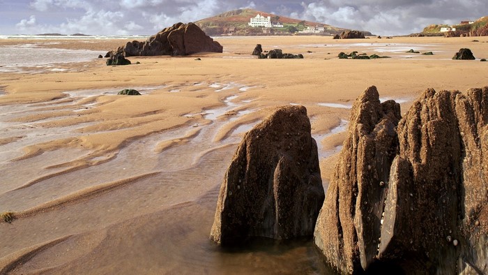 Sandy beach with rocks and a building on a hill