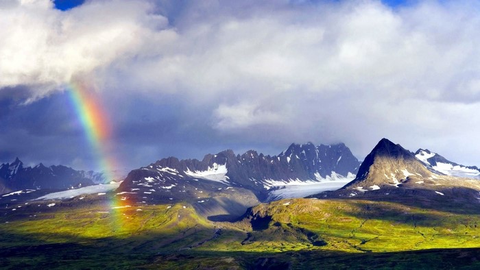 Rainbow over snow-capped mountains and green hills