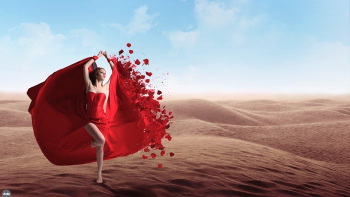 Woman in red dress dissolving into rose petals in desert