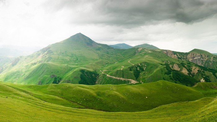 Green mountains with winding roads under cloudy sky