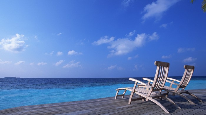 Two empty lounge chairs on a wooden deck by the ocean