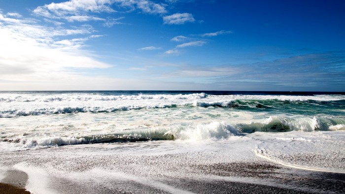Ocean waves crashing on a sandy beach under a blue sky