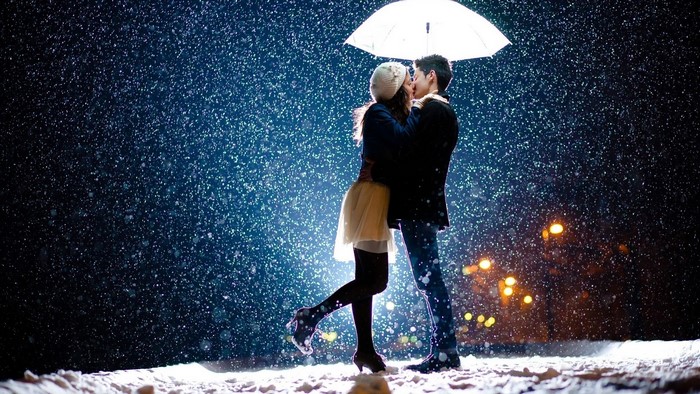 Couple kissing under umbrella in snow