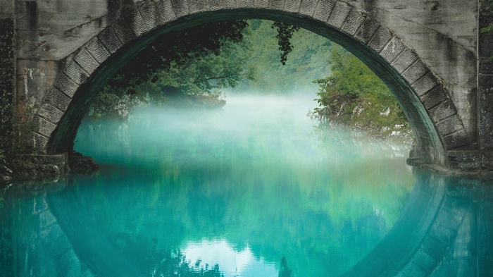Stone bridge over turquoise water with mist