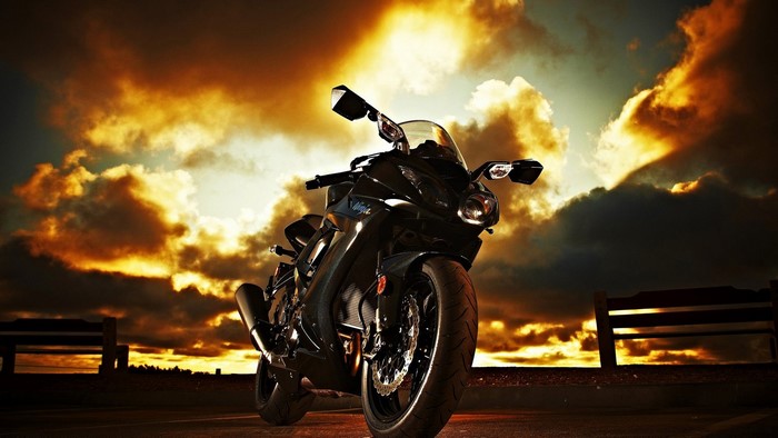 Black motorcycle parked at sunset with dramatic clouds
