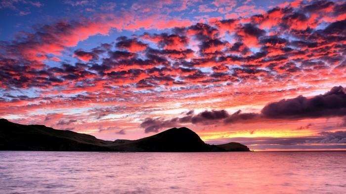 Sunset over the ocean with dramatic clouds and hills