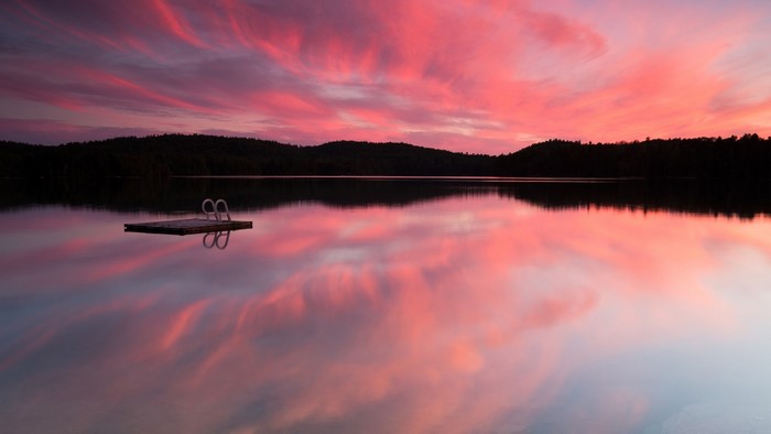 Pink sunset over a Canadian forest lake with a dock