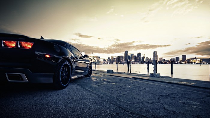 Black Chevrolet Camaro parked by a city skyline at dusk