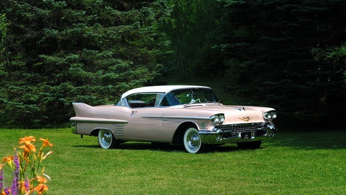 Pink Cadillac parked on grass with trees