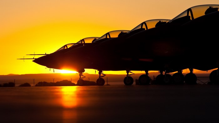 Fighter jets silhouetted against a sunset