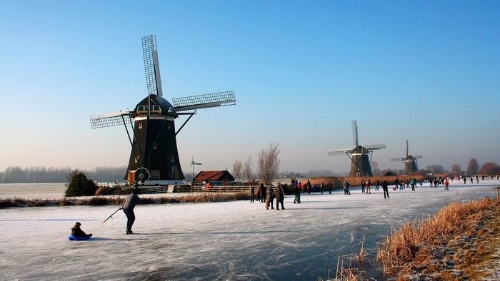 Dutch windmills on a frozen canal with ice skaters