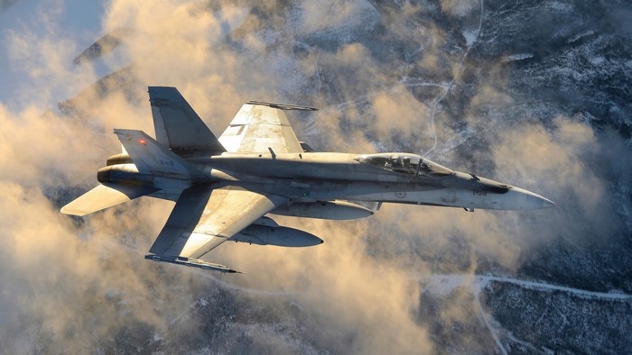 Royal Canadian Air Force CF-18 Hornet flying over snowy mountains