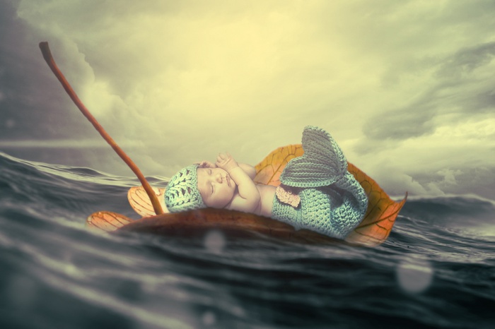 Baby dressed as a mermaid floating on a leaf in the ocean