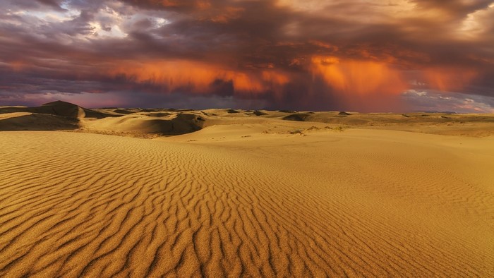 Desert dunes under stormy sunset sky