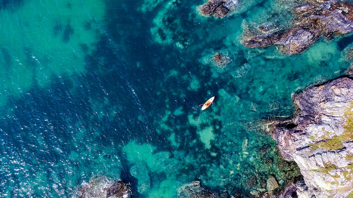 Kayaker in clear turquoise water near rocky shore