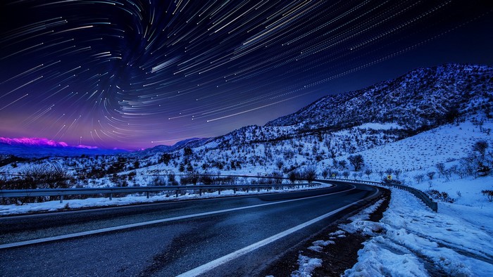 Star trails over a snowy mountain road
