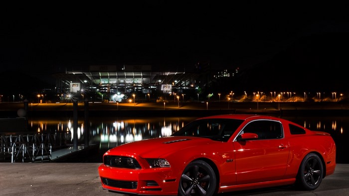 Red Ford Mustang parked by a stadium at night