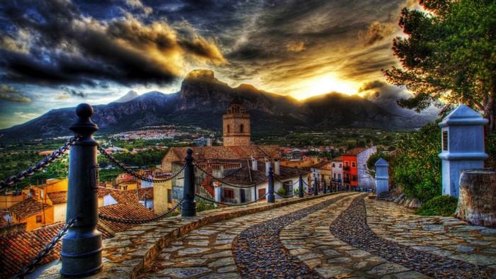 Cobblestone path leading to a town with mountains at sunset