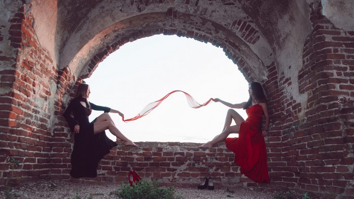Two women in dresses with red scarf in ruins