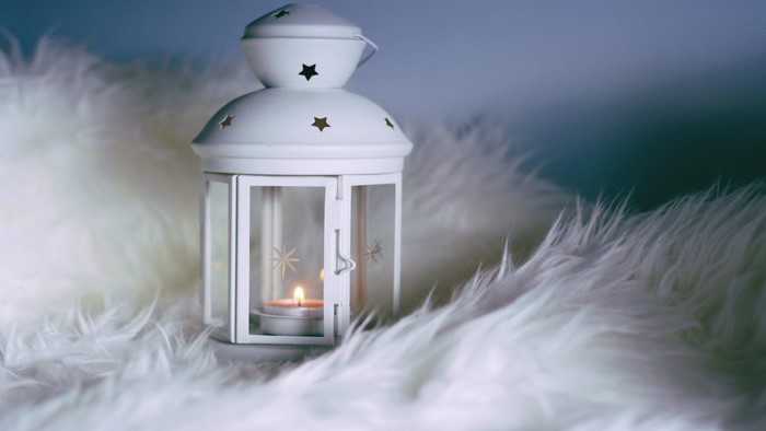 White lantern with lit candle on fluffy rug