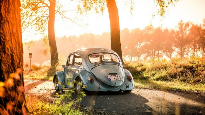 Light blue Volkswagen Beetle on a road at sunset