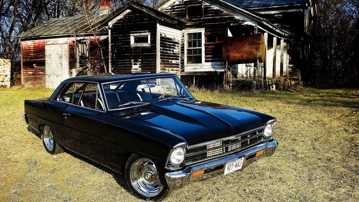 Black Chevrolet Nova parked in front of an abandoned house