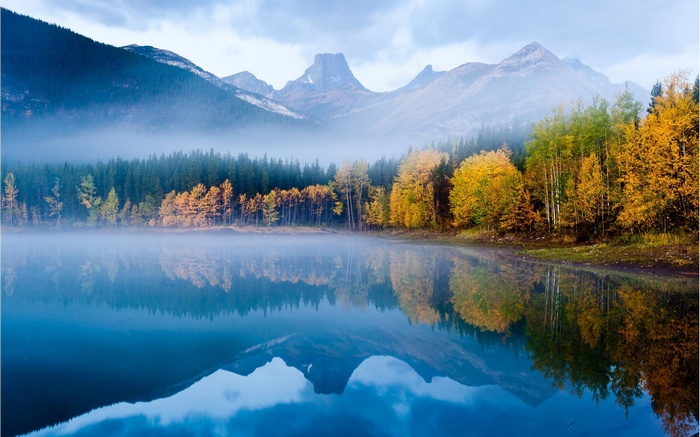 Misty lake reflecting autumn trees and mountains