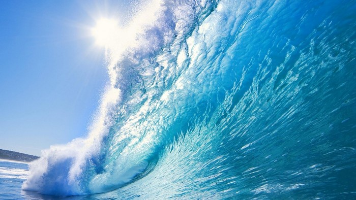 A large ocean wave crashing under the sun
