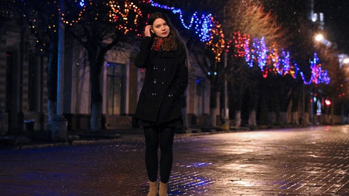 Girl in coat and scarf standing on street at night