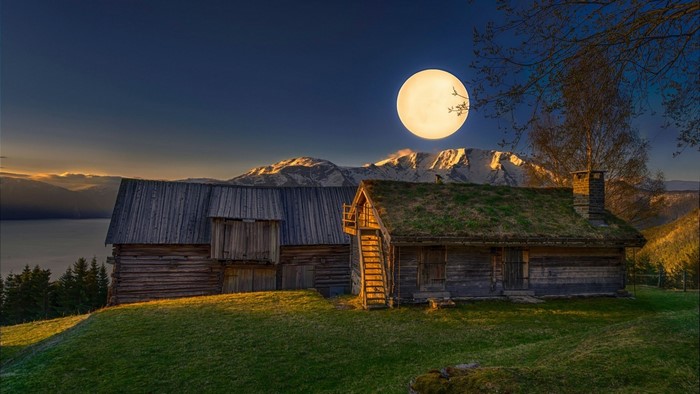 Wooden cabins under a large full moon and mountains