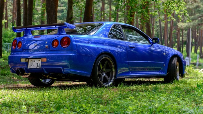 Blue Nissan Skyline R34 GT-R parked in forest