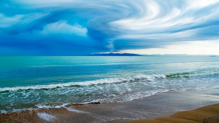 Ocean waves crash on a sandy shore under dramatic clouds