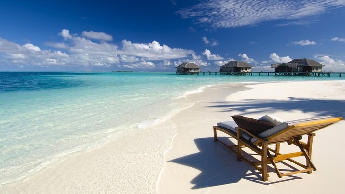 Tropical beach with overwater bungalows and lounge chair